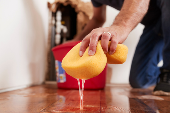 person cleaning flooded floor with yellow sponge and red bucket
