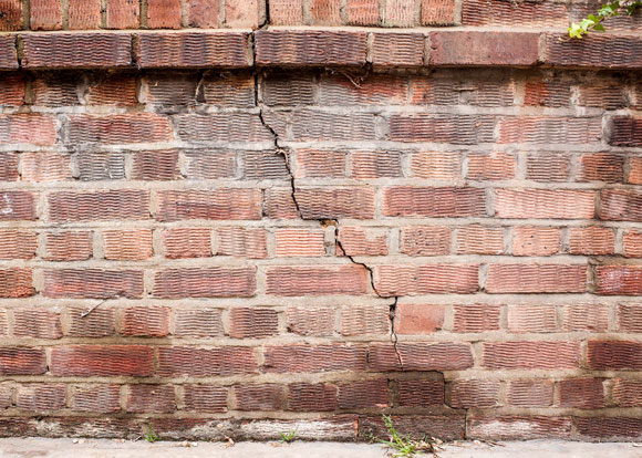 impacted brick wall in red brick with crack from top to bottom at concrete pathway